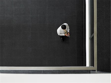 Businessman sending text message in corner of room, overhead view Stock Photo - Premium Royalty-Free, Code: 693-03557261