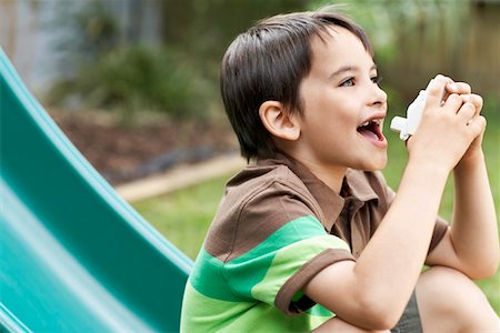 Little boy on slippery slide in park using inhaler Stock Photo - Premium Royalty-Free, Code: 693-03564885