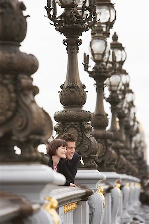 paris streetlight - Couple looking over bridge through streetlights Stock Photo - Premium Royalty-Free, Code: 693-03565457