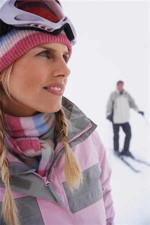 ski goggles mature not senior - Woman standing on ski slope, man on skis in background Stock Photo - Premium Royalty-Free, Code: 693-03565719