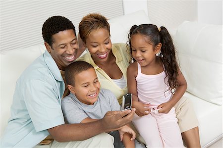 Family sitting on sofa looking at picture on camera phone Stock Photo - Premium Royalty-Free, Code: 693-03706986