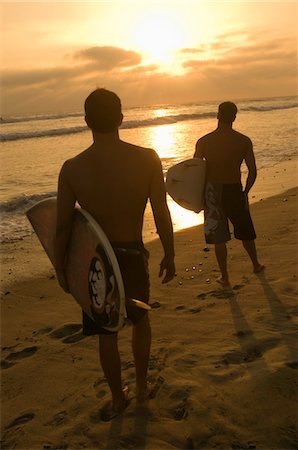 Two surfers standing on beach, holding surfboards, watching sunset, back view Stock Photo - Premium Royalty-Free, Code: 693-03707031