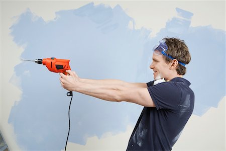 drilling wall - Man pointing drill in front of half painted wall, side view Stock Photo - Premium Royalty-Free, Code: 693-03707955