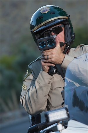 Traffic policeman sits on motorcycle looking through pseedometer Foto de stock - Sin royalties Premium, Código: 693-03782766