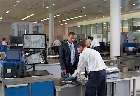 Garde de sécurité vérifiant des bagages les hommes d'affaires à l'aéroport Photographie de stock - Rights-Managed, Code: 700-05821740