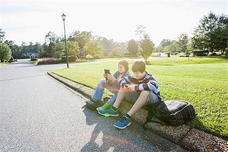 Two Boys Sitting on Neighbourhood Curb with Handheld Electronics Foto de stock - Con derechos protegidos, Código: 700-06439142