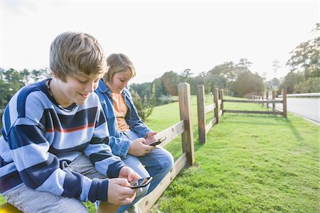 simsearch:700-06439143,k - Two Boys with Handheld Electronics Sitting on Roadside Fence Photographie de stock - Rights-Managed, Code: 700-06439150