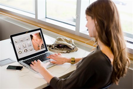 Woman in library using a laptop to shop online for jewelry while listening to music with her smartphone. Stockbilder - Lizenzpflichtiges, Bildnummer: 700-06553289
