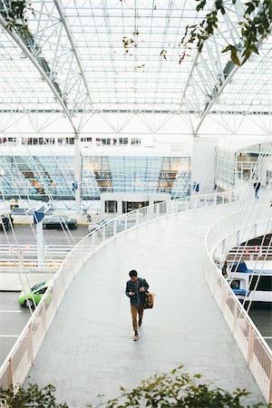 Overview of Man Checking Cell Phone while Walking on Aerial Walkway at Airport Stock Photo - Rights-Managed, Code: 700-06701844