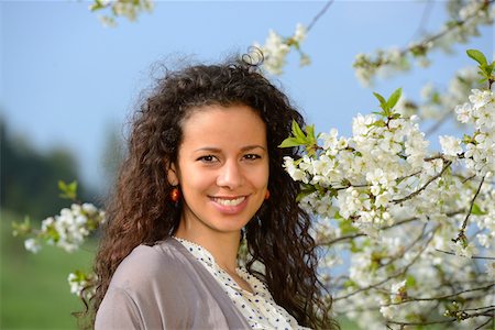 Portrait of a young woman with dark, curly hair standing beside a flowering cherry tree in spring, Germany Stock Photo - Rights-Managed, Code: 700-06808850