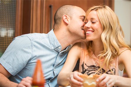 Young man kissing young woman on cheek, sitting and eating in home, Canada Foto de stock - Con derechos protegidos, Código: 700-07237598