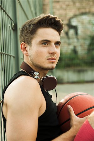 simsearch:600-06899940,k - Close-up portrait of young man sitting on ground with basketball, wearing headphones around neck at fenced-in basketball court, Germany Foto de stock - Con derechos protegidos, Código: 700-07237993