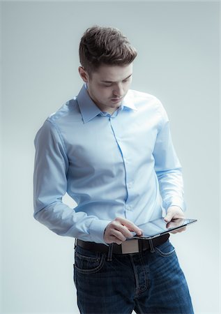 Young man looking down at tablet computer, studio shot on white background Stockbilder - Lizenzpflichtiges, Bildnummer: 700-07278869
