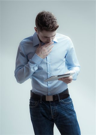 Young man looking down at tablet computer, studio shot on white background Stockbilder - Lizenzpflichtiges, Bildnummer: 700-07278870