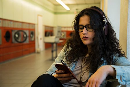 phone young white woman - Teenage girl sitting in laundromat, wearing headphones and listening to music on smart phone, Germany Photographie de stock - Rights-Managed, Code: 700-07310981