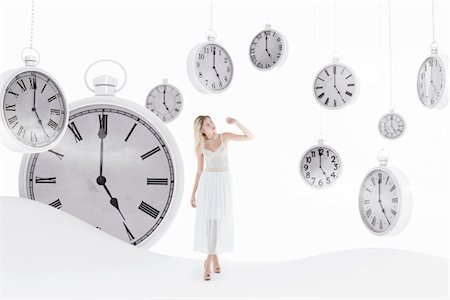 Young woman wearing white dress, standing in abstract landscape with pocket watches hanging in sky, studio shot Stockbilder - Lizenzpflichtiges, Bildnummer: 700-07487679