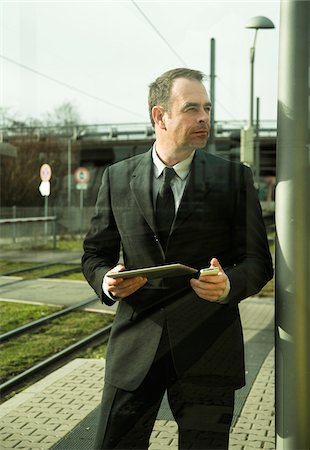 Portrait of businessman holding cell phone and tablet computer, standing at train station outdoors, Mannheim, Germany Photographie de stock - Rights-Managed, Code: 700-07529273
