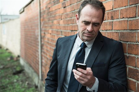 simsearch:600-07110820,k - Portrait of businessman standing next to brick wall outdoors, looking at cell phone, Germany Photographie de stock - Rights-Managed, Code: 700-07529282