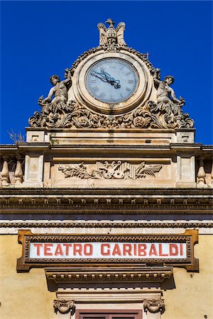 simsearch:700-08723111,k - Ornate clock on the roof of the Garibaldi Theatre (Teatro Garibaldi) against a blue sky in Modica in the Province of Ragusa in Sicily, Italy Foto de stock - Con derechos protegidos, Código: 700-08723125