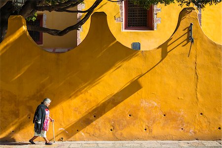 Senior woman walking with cane along street infront of yellow stucco wall in San Miguel de Allende, Mexico. Stock Photo - Rights-Managed, Code: 700-09071034