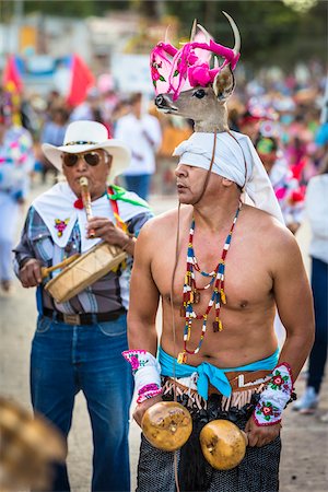 Indigenous tribal dancer wearing a deer head on his headdress and a musician playing the flute in the background in the St Michael Archangel Festival parade in San Miguel de Allende, Mexico Foto de stock - Con derechos protegidos, Código: 700-09088092