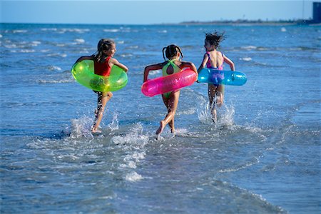 Back View of Girls in Swimwear Running on Beach with Inner Tubes Stock Photo - Rights-Managed, Code: 700-00037111