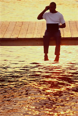 Man Sitting on Dock with Cell Phone and Laptop at Sunset Stock Photo - Rights-Managed, Code: 700-00054925