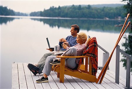 Mature Couple Sitting in Chairs On Dock with Mugs and Laptop Stock Photo - Rights-Managed, Code: 700-00055383