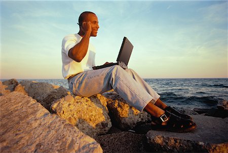 Man Sitting on Rocks near Water Using Cell Phone and Laptop Stock Photo - Rights-Managed, Code: 700-00055573