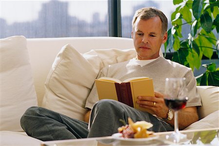Mature Man Sitting on Sofa Reading Book with Wine and Cheese Stock Photo - Rights-Managed, Code: 700-00055927