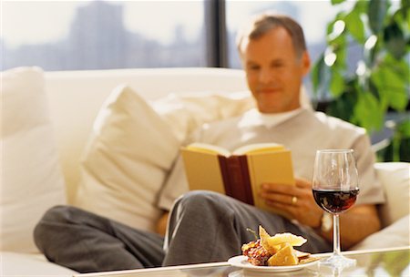 Mature Man Sitting on Sofa Reading Book with Wine and Cheese Stock Photo - Rights-Managed, Code: 700-00055928