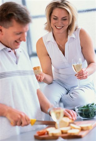 Couple Preparing Food in Kitchen With Glasses of Wine Foto de stock - Con derechos protegidos, Código: 700-00055953