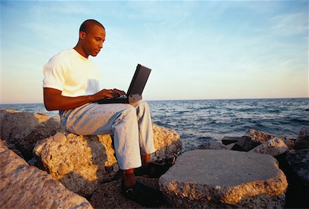 Man Sitting on Rocks, Using Laptop Computer near Water Stock Photo - Rights-Managed, Code: 700-00053824
