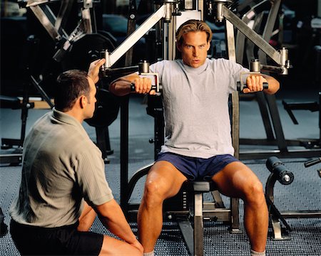 posição - Man Using Exercise Machine in Gym With Man Spotting Foto de stock - Direito Controlado, Número: 700-00053927
