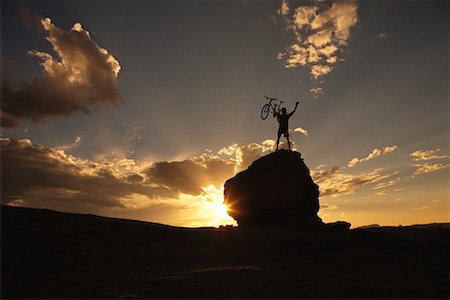 Silhouette of Man Standing on Rock, Holding Bike at Sunset Stock Photo - Rights-Managed, Code: 700-00064008