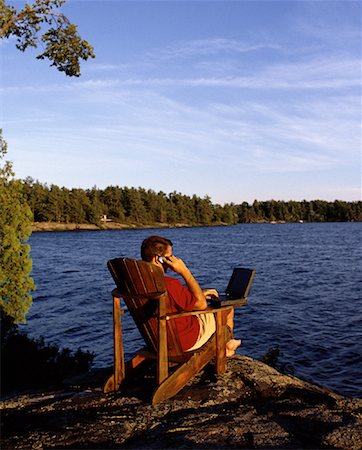Man Sitting in Chair near Lake Using Laptop and Cell Phone Stock Photo - Rights-Managed, Code: 700-00067928