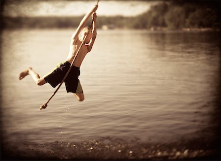 Boy Hanging from Rope Swing over Water Stock Photo - Rights-Managed, Code: 700-00062442