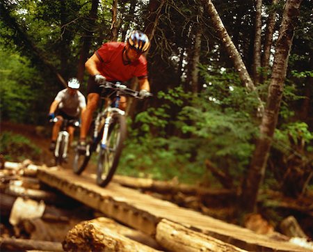 simsearch:600-00021728,k - Hommes Riding Mountain Bikes sur un chemin en bois dans la forêt Photographie de stock - Rights-Managed, Code: 700-00063170