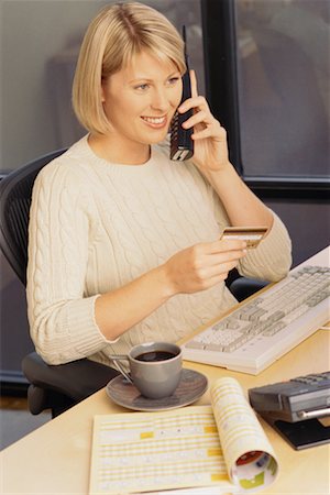 Businesswoman Sitting at Desk Using Phone, Holding Credit Card Stock Photo - Rights-Managed, Code: 700-00074083