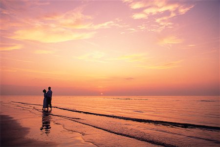 simsearch:700-00152780,k - Mature Couple Embracing en Surf sur la plage au coucher du soleil Photographie de stock - Rights-Managed, Code: 700-00077506