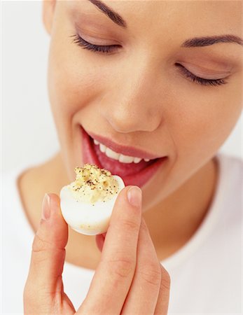 eggs with face - Woman Eating Deviled Egg Stock Photo - Rights-Managed, Code: 700-00078004