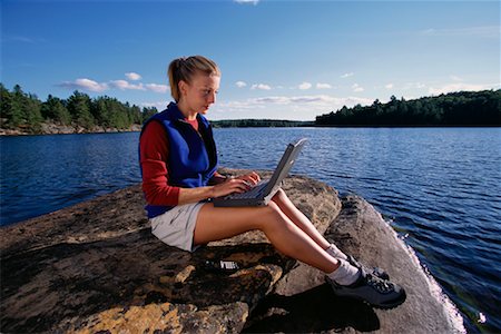 Woman Sitting on Rock in Lake Using Laptop Computer Haliburton, Ontario, Canada Stock Photo - Rights-Managed, Code: 700-00071229