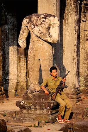 preah khan temple - Man Sitting by Statue, Holding Gun at Preah Khan Temple Siem Reap, Cambodia Fotografie stock - Rights-Managed, Codice: 700-00086617