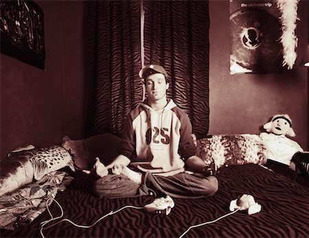 Portrait of Young Man Sitting in Lotus Position with Video Game Controllers on Bed Stock Photo - Rights-Managed, Code: 700-00080731