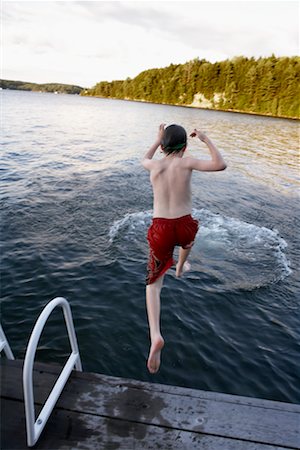 Boy Jumping off Dock into Lake Foto de stock - Direito Controlado, Número: 700-00651504