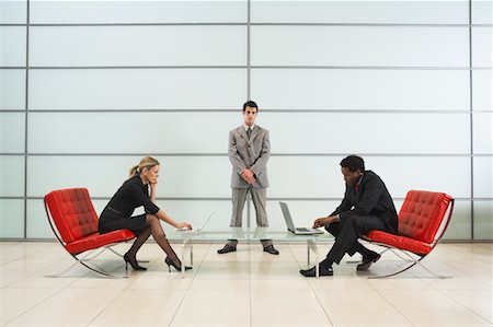 photo poses for suited dress - Two Business People using Laptops, with Businessman Standing by Wall Stock Photo - Rights-Managed, Code: 700-00681369