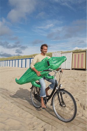 Man Riding Bicycle and Carrying Inflatable Crocodile on Beach Foto de stock - Con derechos protegidos, Código: 700-01042790