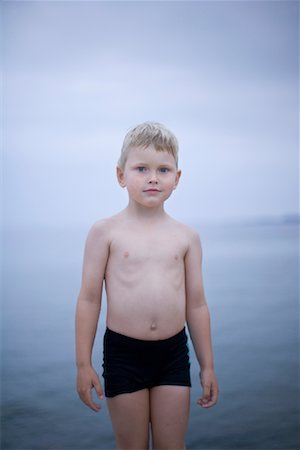 Boy Standing on Beach in Swim Shorts Foto de stock - Con derechos protegidos, Código: 700-01828731