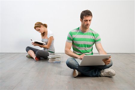 Jeune homme à l'aide d'ordinateur portable tandis que la jeune femme se lit Photographie de stock - Rights-Managed, Code: 700-02130550
