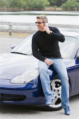 Man Sitting on Car Hood, Talking on Cell Phone Foto de stock - Direito Controlado, Número: 700-02231985
